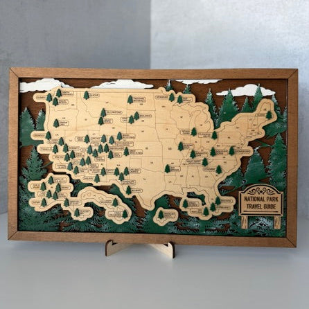 A 3D layered wooden map of the United States, featuring National Park Travel Route highlights, displayed on a small stand against a gray background.