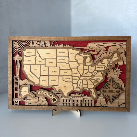 A rectangular wooden USA travel map plaque with laser-cut state outlines and iconic landmarks, displayed on a small stand against a light gray background.