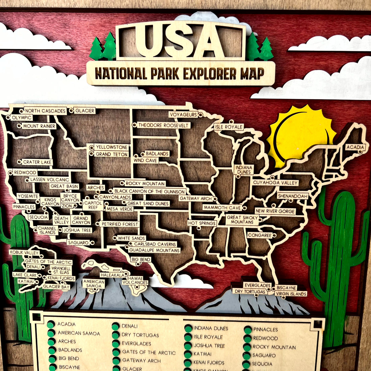 A handcrafted wooden USA National Park Explorer Map featuring carved state outlines, labeled park names, a yellow sun, green cacti, and a red wood-grain background.