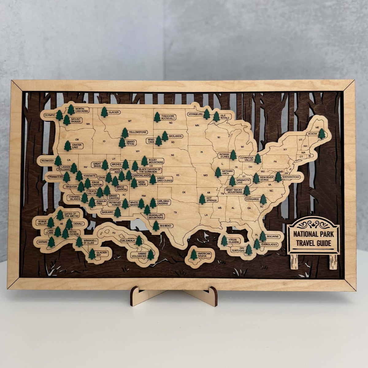 A rectangular wooden map plaque of the United States National Parks, displayed on a small wooden stand against a gray background.