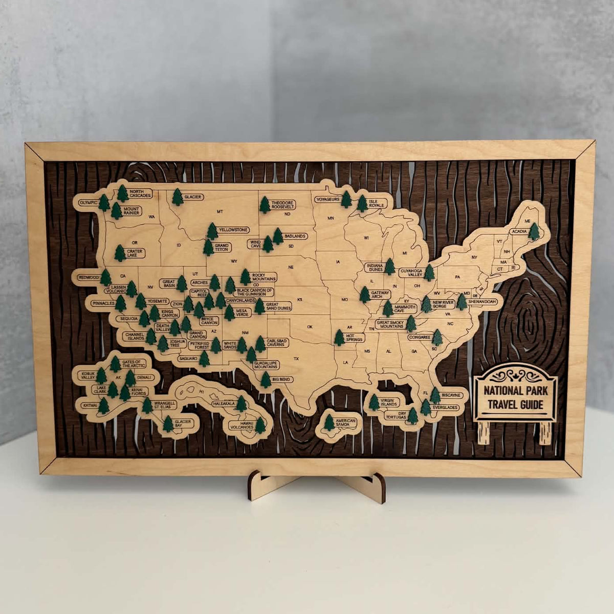 A rectangular wooden map plaque of the United States highlighting National Parks, displayed on a small wooden stand against a gray background.